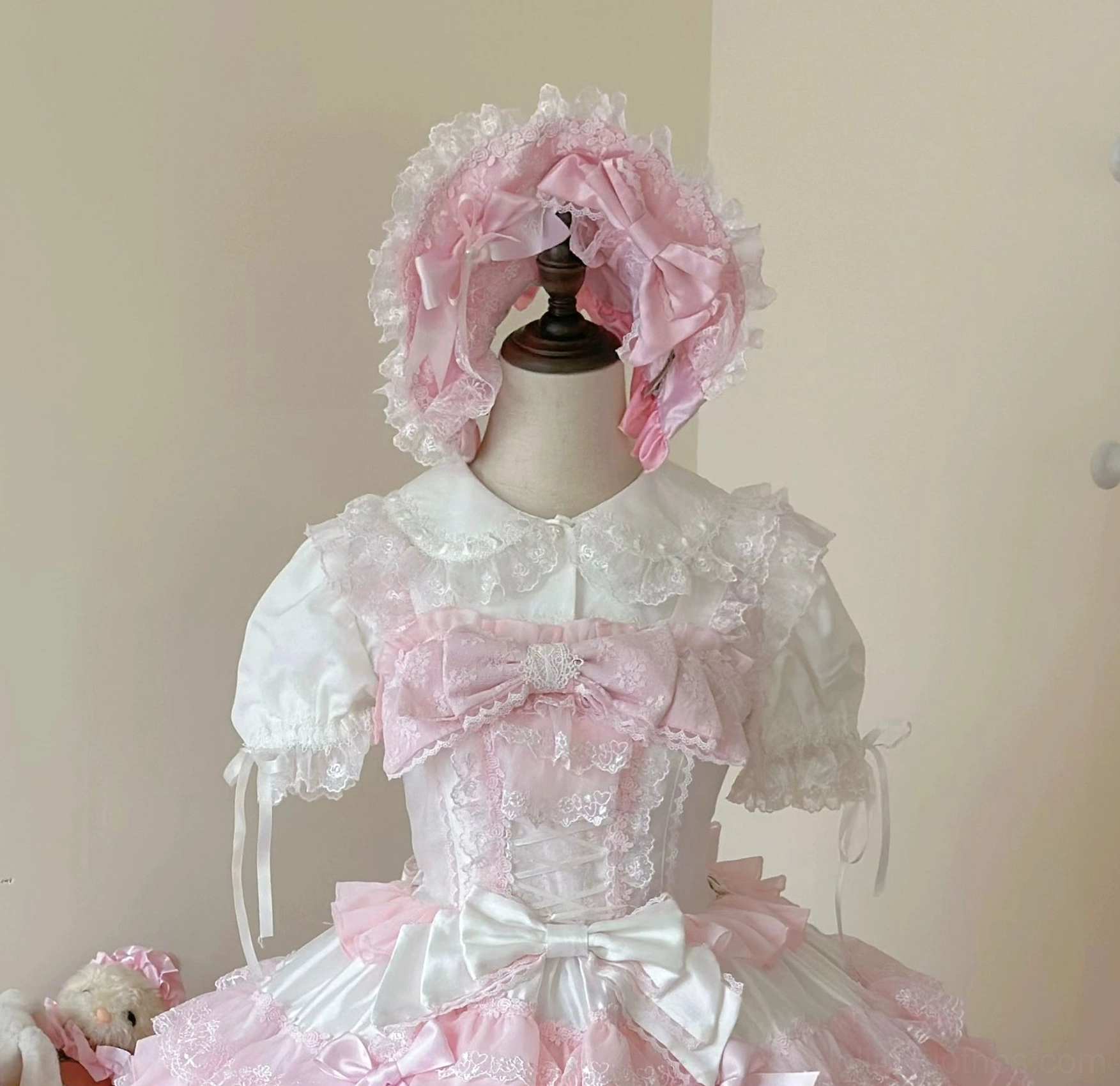 Close-up detail of white and pink lolita dress showing lace trim hem ruffles and satin bow embellishments craftsmanship