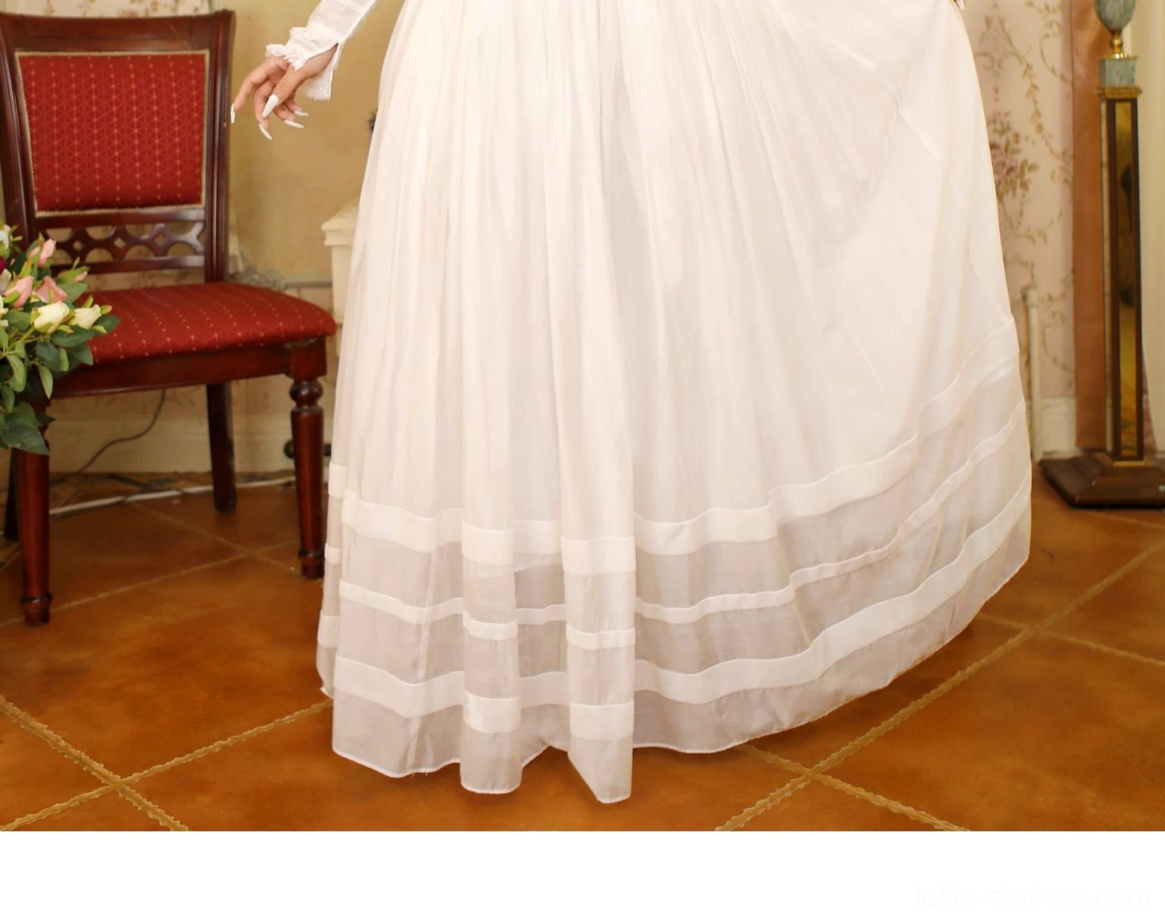 Low front full view of white pleated Lolita skirt with multiple horizontal sheer trim bands at hem and full flowy pleated silhouette in cotton fabric, vintage room with red upholstered chairs interior