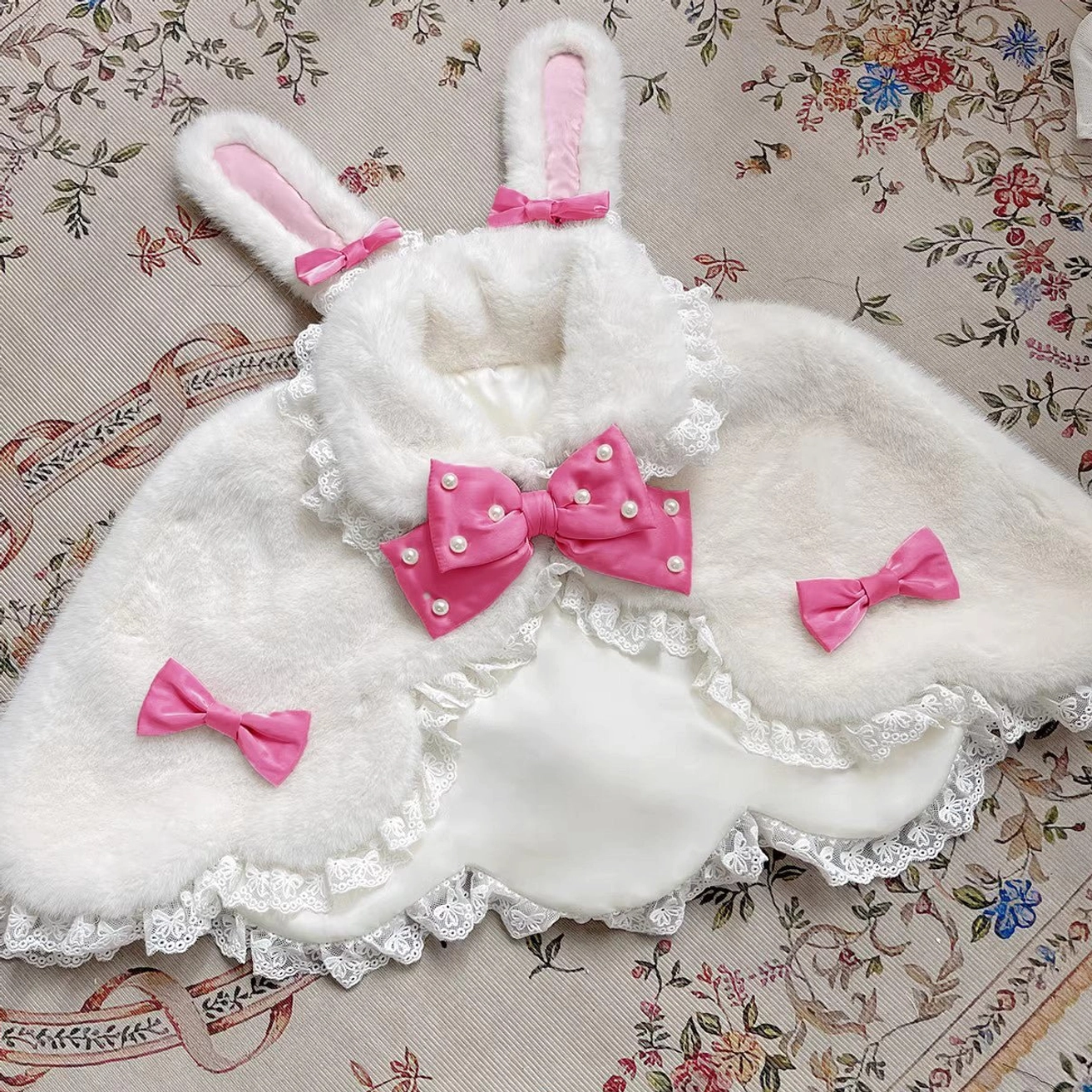 White plush Lolita cape with strong pink pearl-studded bow and rabbit ears design flat lay presentation