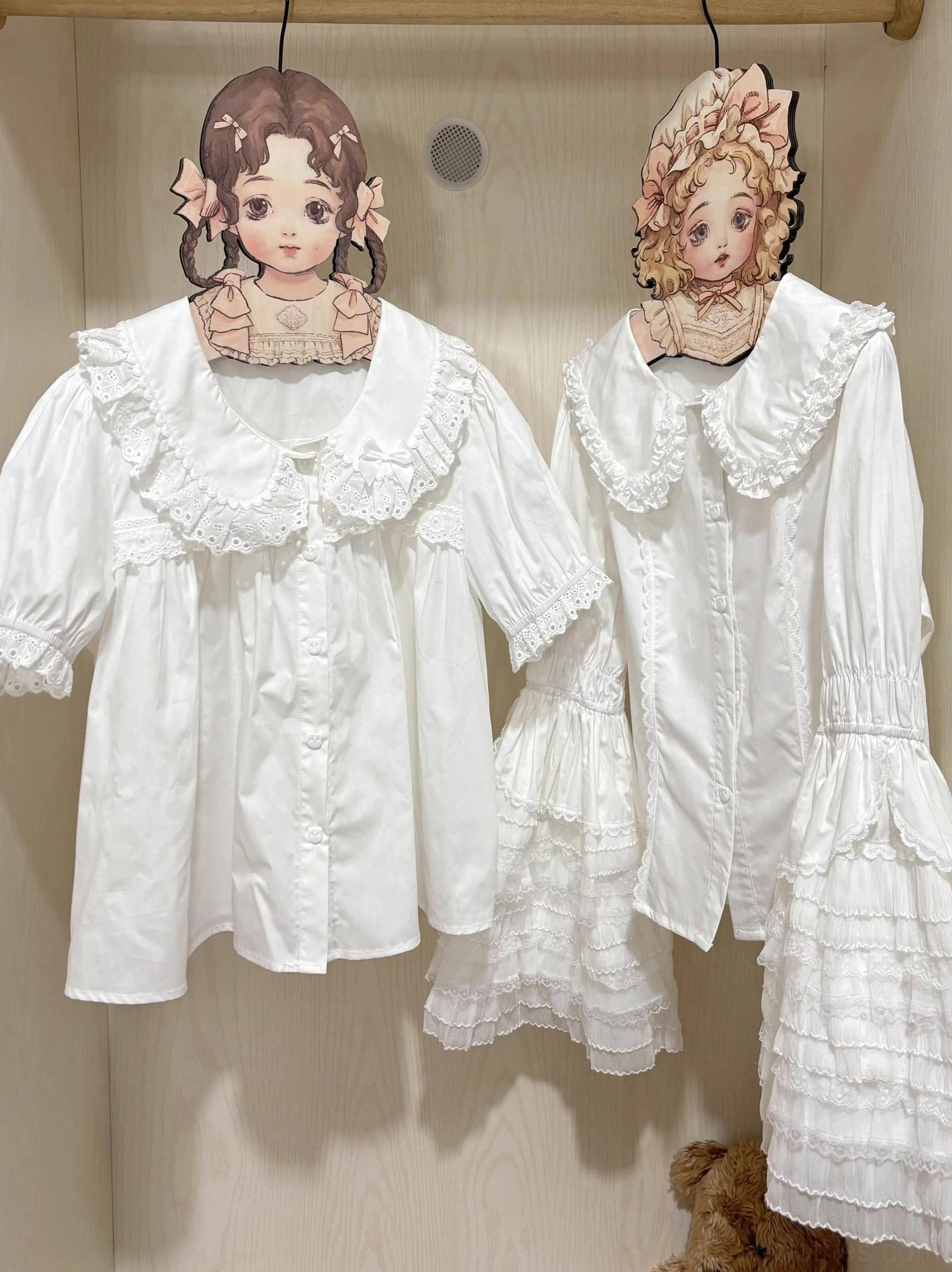 White princess-sleeve lolita blouse with double-layered scalloped lace peter pan collar and ruffled long sleeves displayed on wooden hanger with cartoon girl clothing rack, embroidered lace trim details