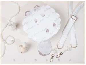 White ragdoll kawaii cat shoulder bag flat lay with pearl chains and rabbit ornaments, displaying cat face embroidery and scalloped edge design on studio background
