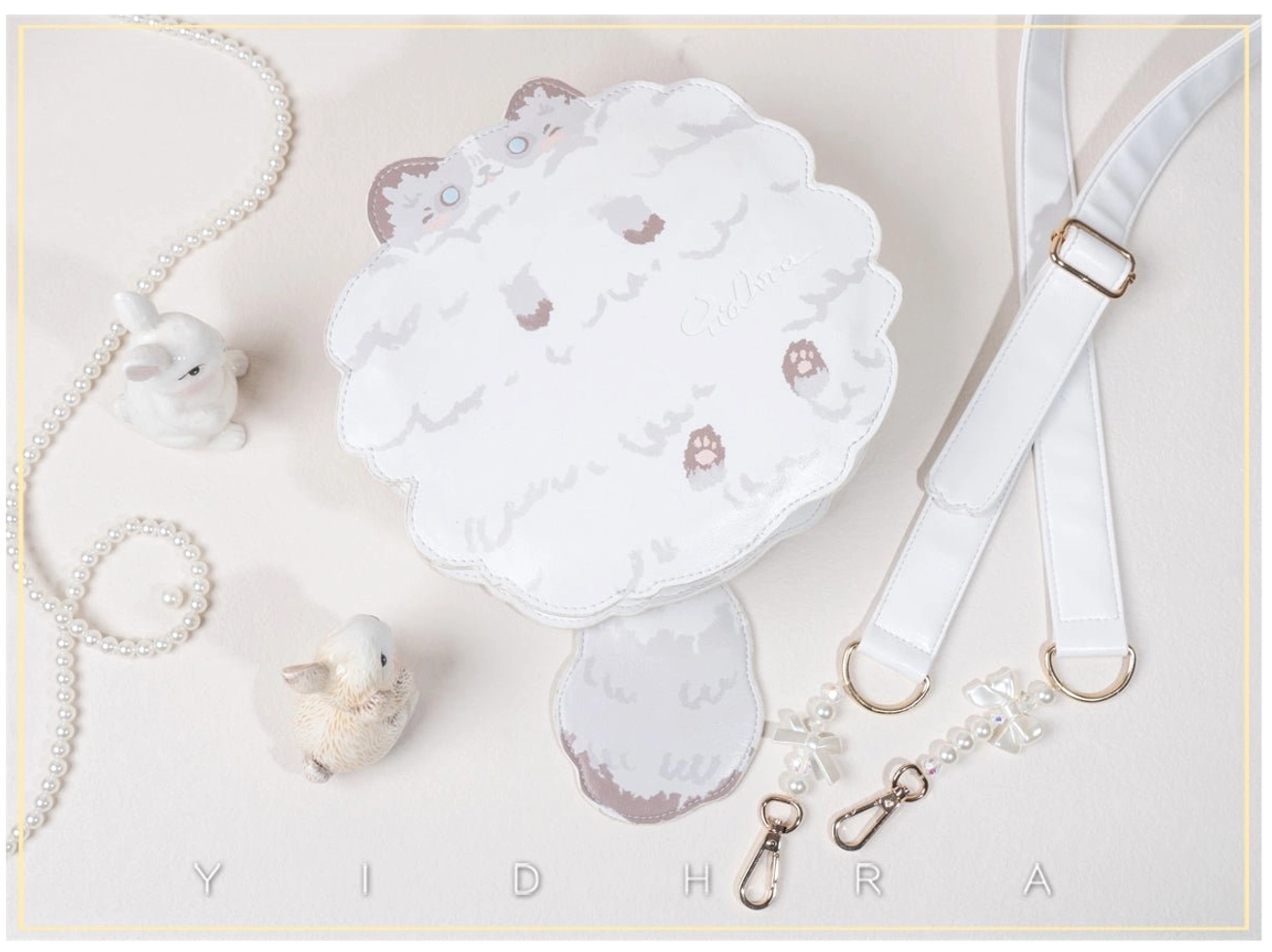 White ragdoll kawaii cat shoulder bag flat lay with pearl chains and rabbit ornaments, displaying cat face embroidery and scalloped edge design on studio background
