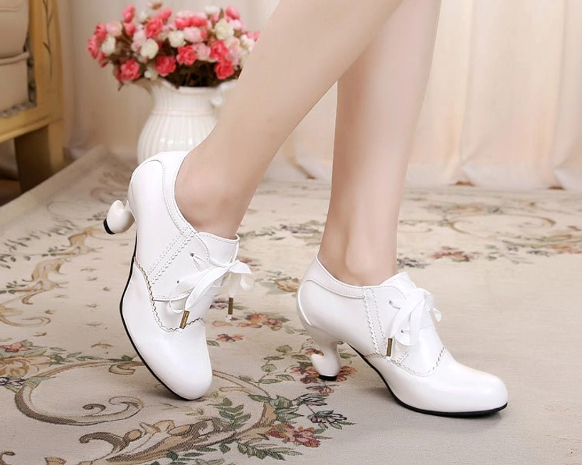 Pure white retro lace-up Lolita high heel shoes with smooth bright white surface, curved spool heel, and ribbon lace closures with metal aglets, side view on vintage floral rug