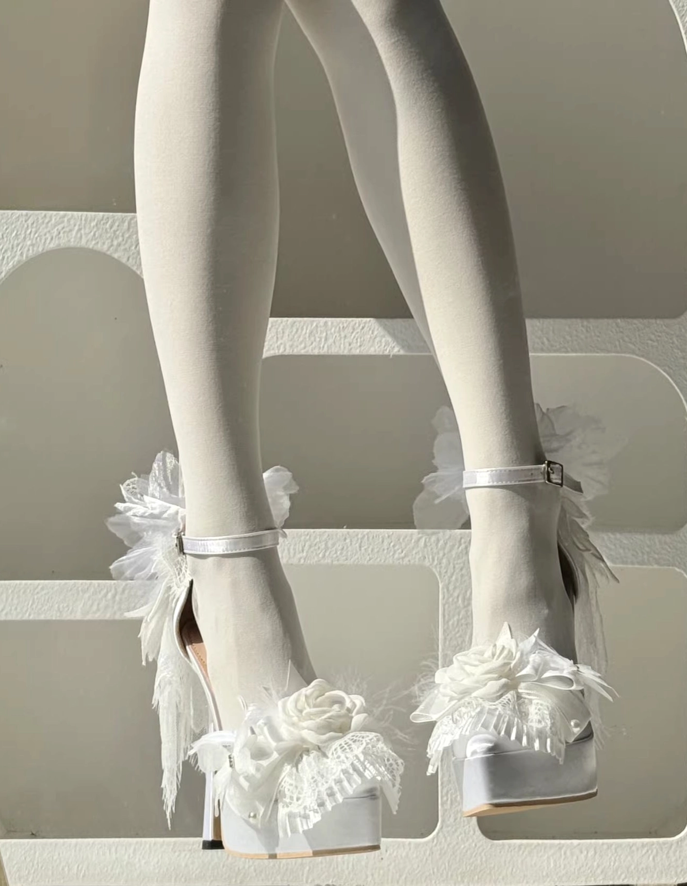 White romantic lolita platform high heel shoes featuring lace flower and feather trims, satin upper, ankle buckle strap, chunky platform heel, side static shot on mannequin with white sheer stockings