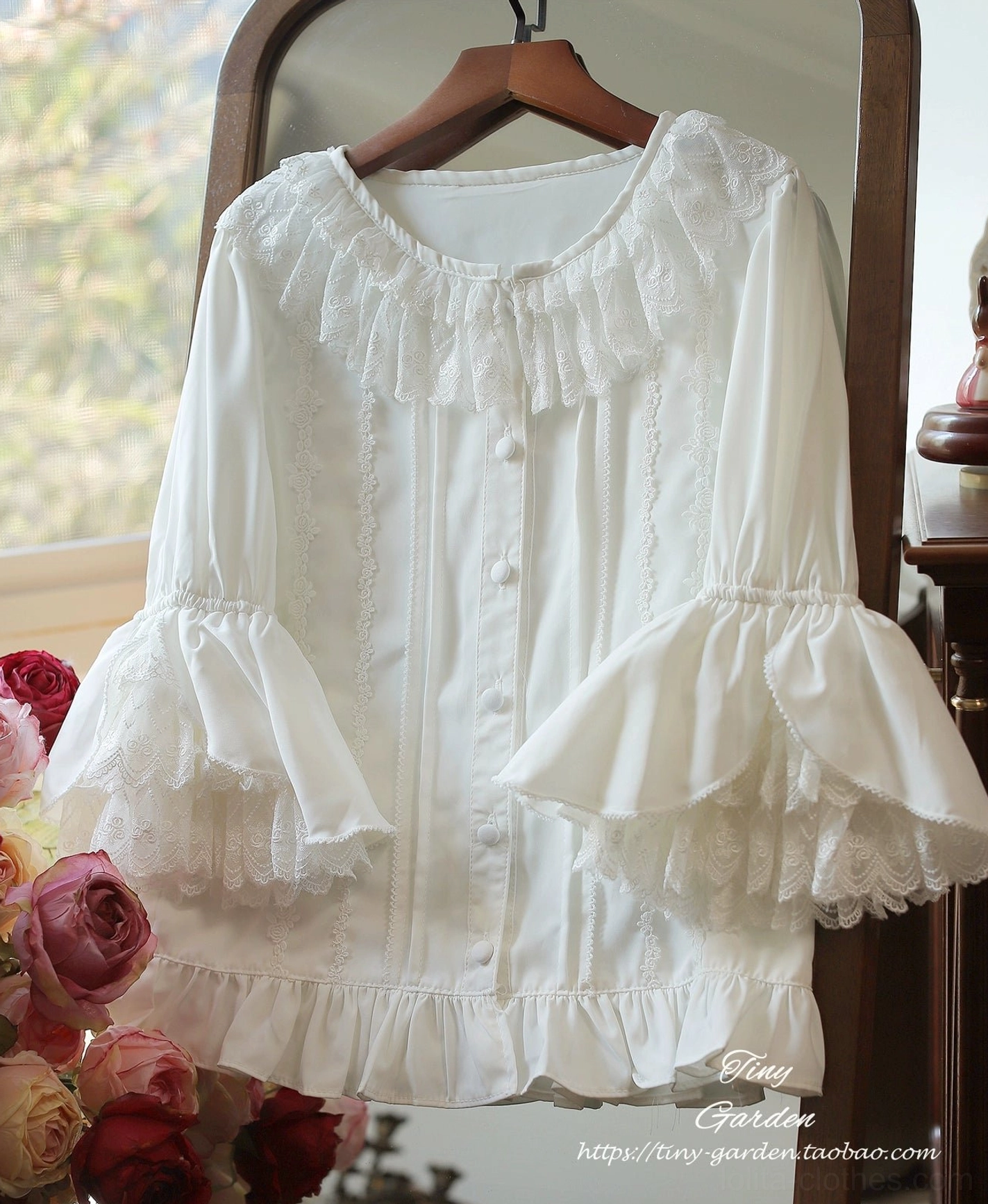 White vintage ruffled lolita blouse with round ruffled collar and layered bell sleeves, hanging front display with retro mirror and flower background, featuring delicate lace trim detailing