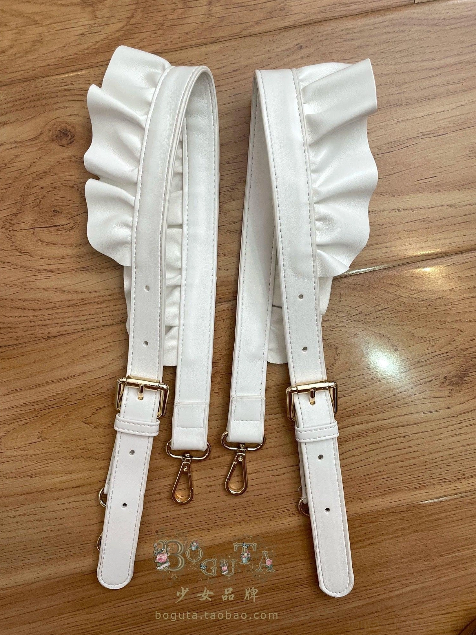 White ruffled PU leather lolita bag shoulder straps pair featuring smooth faux leather material and gold-tone metal buckles and clasps on warm wooden tabletop