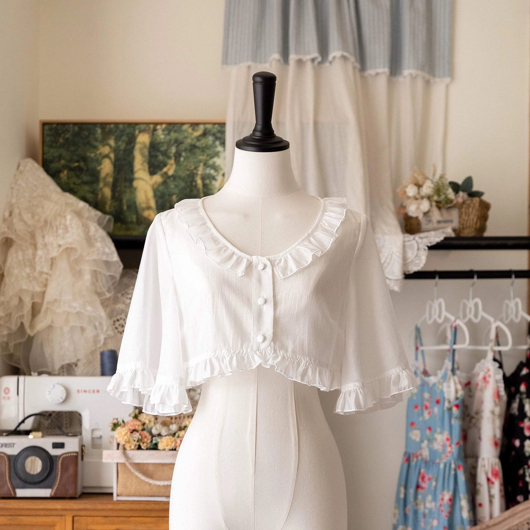 White ruffled Tencel cropped cardigan front view on dress form, vintage studio setting with sewing details, showing delicate flutter sleeves and button closure for sweet Lolita layering