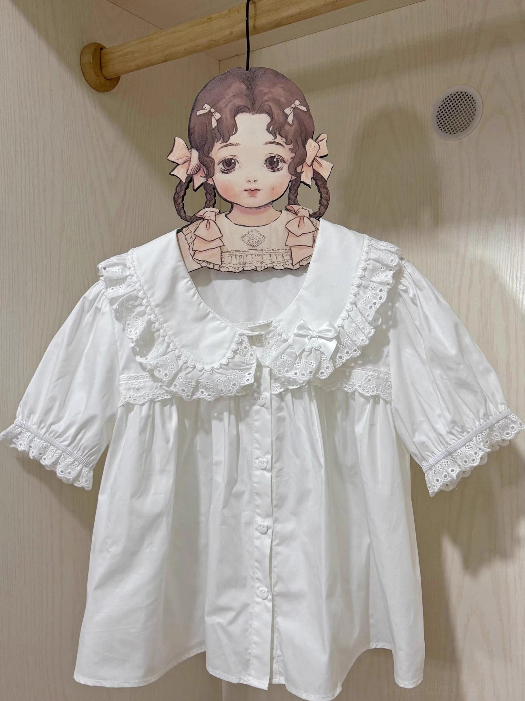 Short-sleeve white peter pan collar lolita blouse front hanging display on wooden wardrobe with cartoon girl clothing hanger, embroidered lace trim on collar and puff cuffs, pure white cotton fabric