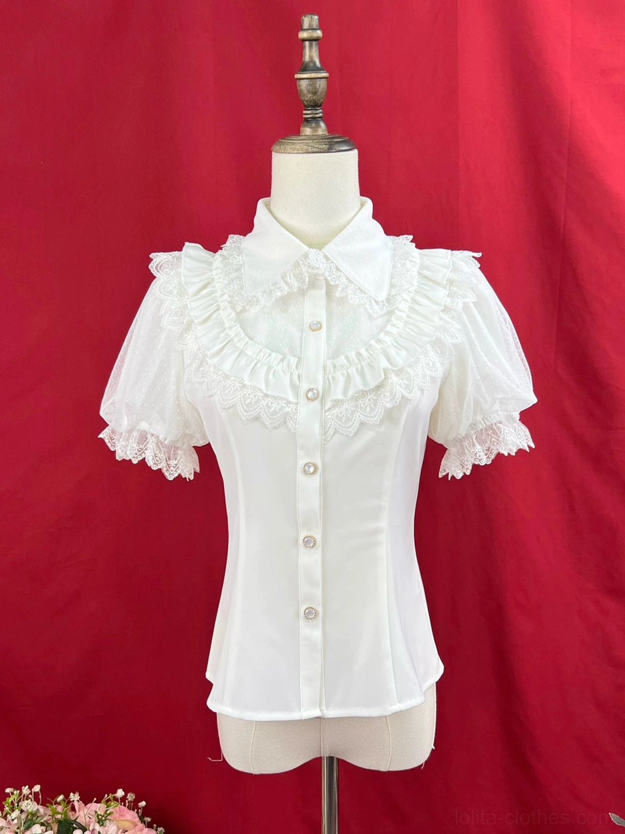 White short-sleeve sweet lolita blouse with peter pan collar front button closures chest ruffled lace trim and short puff sleeves with lace edging on dress form red studio backdrop flowers