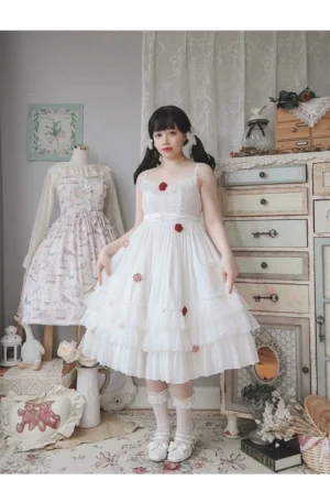 White plus-size spring Lolita JSK dress with spaghetti straps, tiered ruffled midi skirt, and red rose applique decorations worn by model with twin black braids in vintage cottage bedroom, front full-body standing view