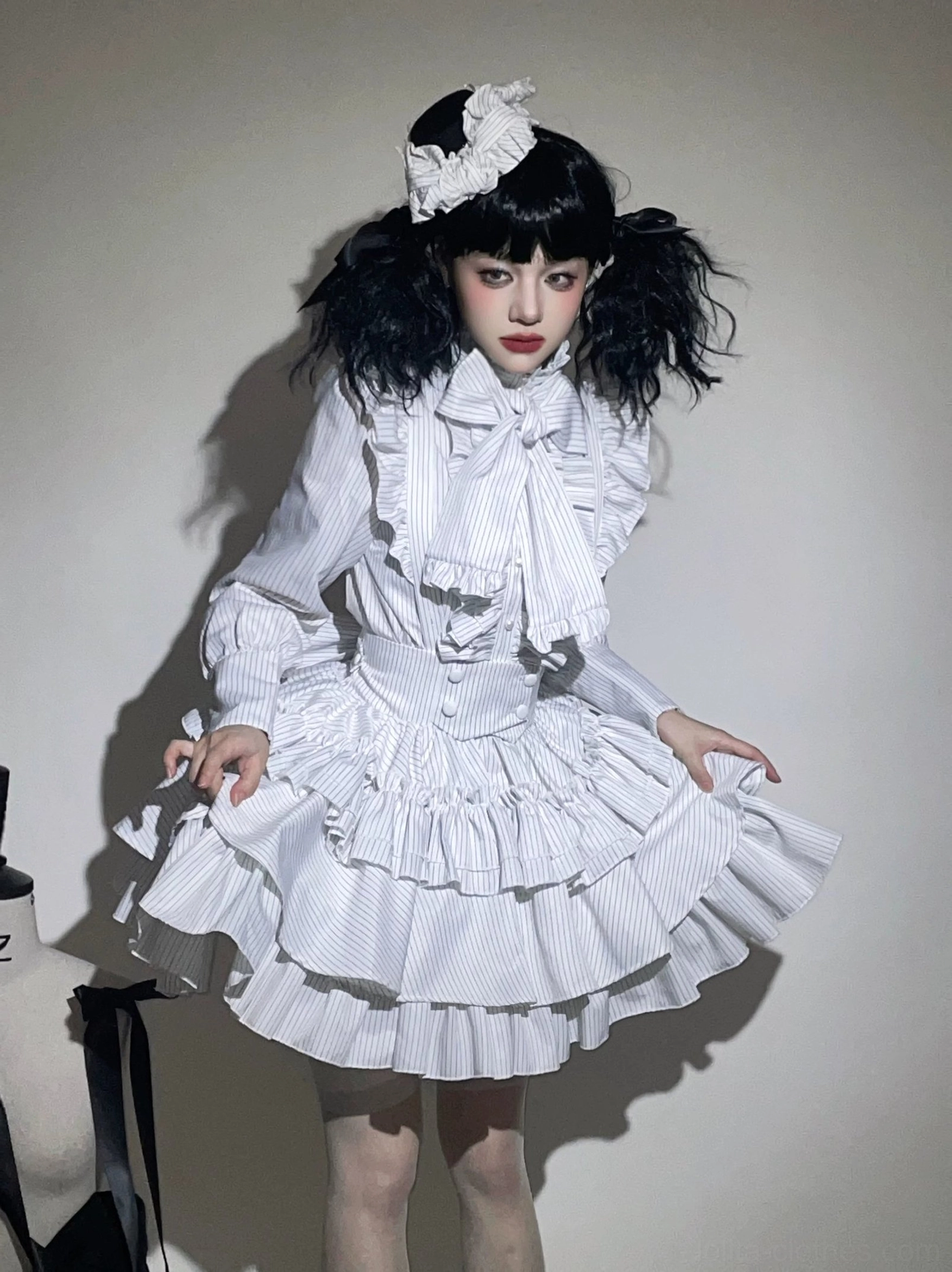White striped gothic lolita ensemble front standing perspective, featuring ruffled high collar with bow tie and multi-layered tiered mini skirt on model with white hair ornament