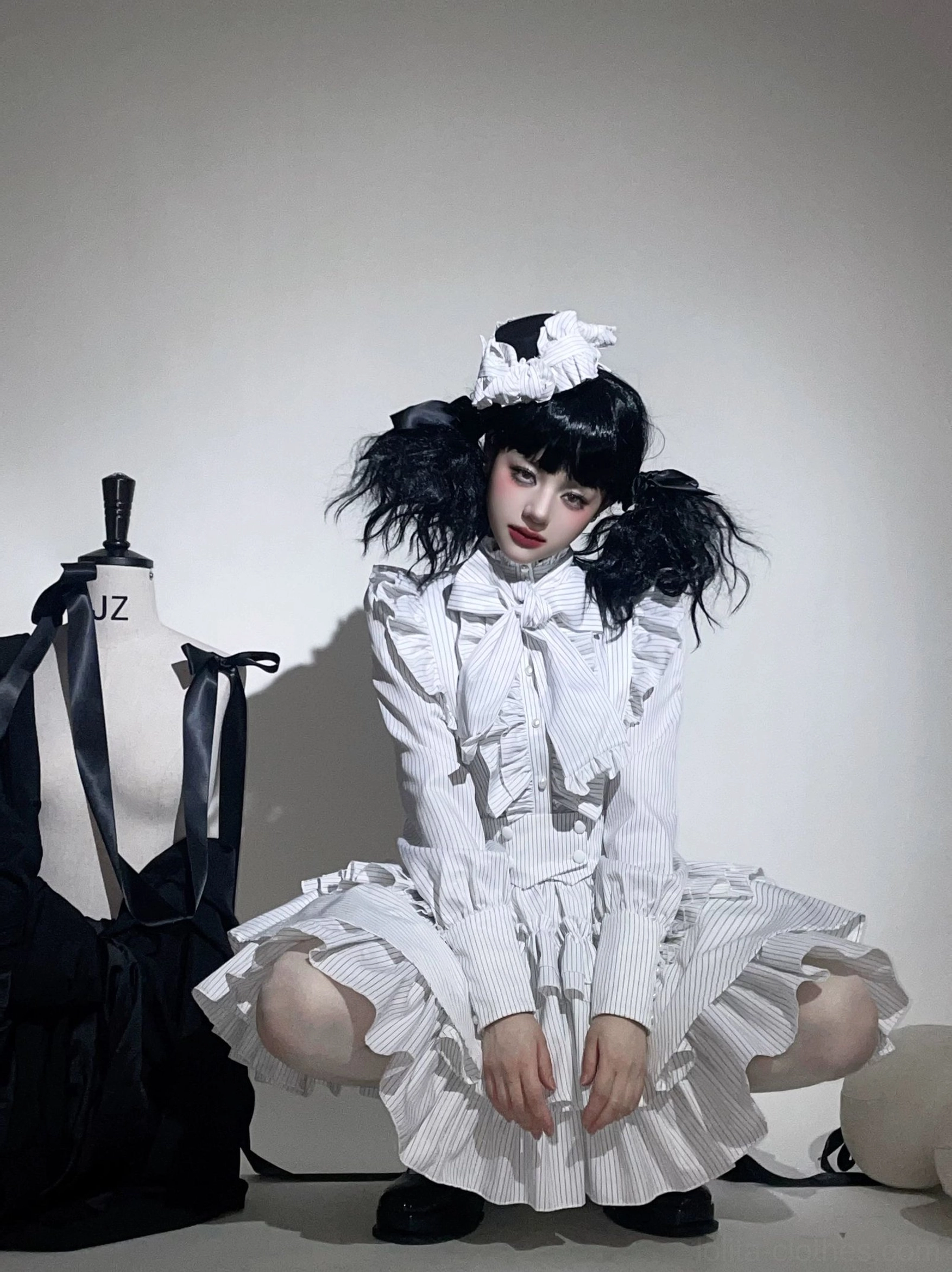 White striped gothic lolita suit on kneeling model front eye-level view, featuring elaborate ruffled collar and tiered skirt, bow neck tie, all-white stripe print design