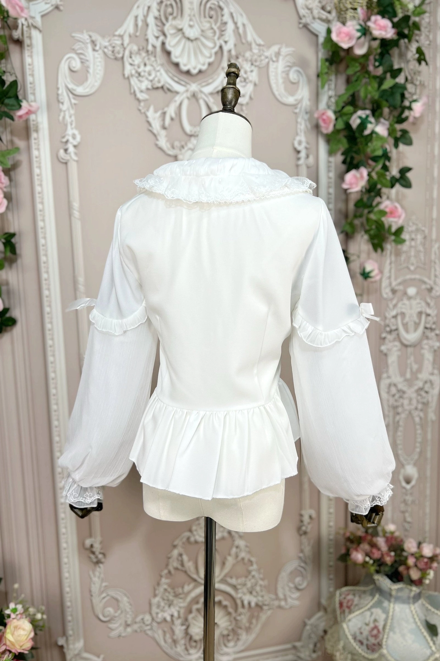 Back view of white sweet Lolita blouse on dress form mannequin displaying ruffled back hem, double-layered puff sleeves with ruffled cuffs and overall silhouette - rear perspective vintage backdrop