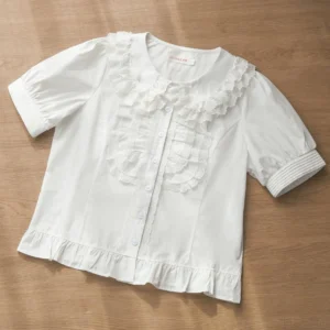 White short-sleeve Sweet Lolita blouse with multi-layered lace Peter Pan collar, front ruffled button placket, puff sleeves with cuff trim, and ruffled hem on flat lay display