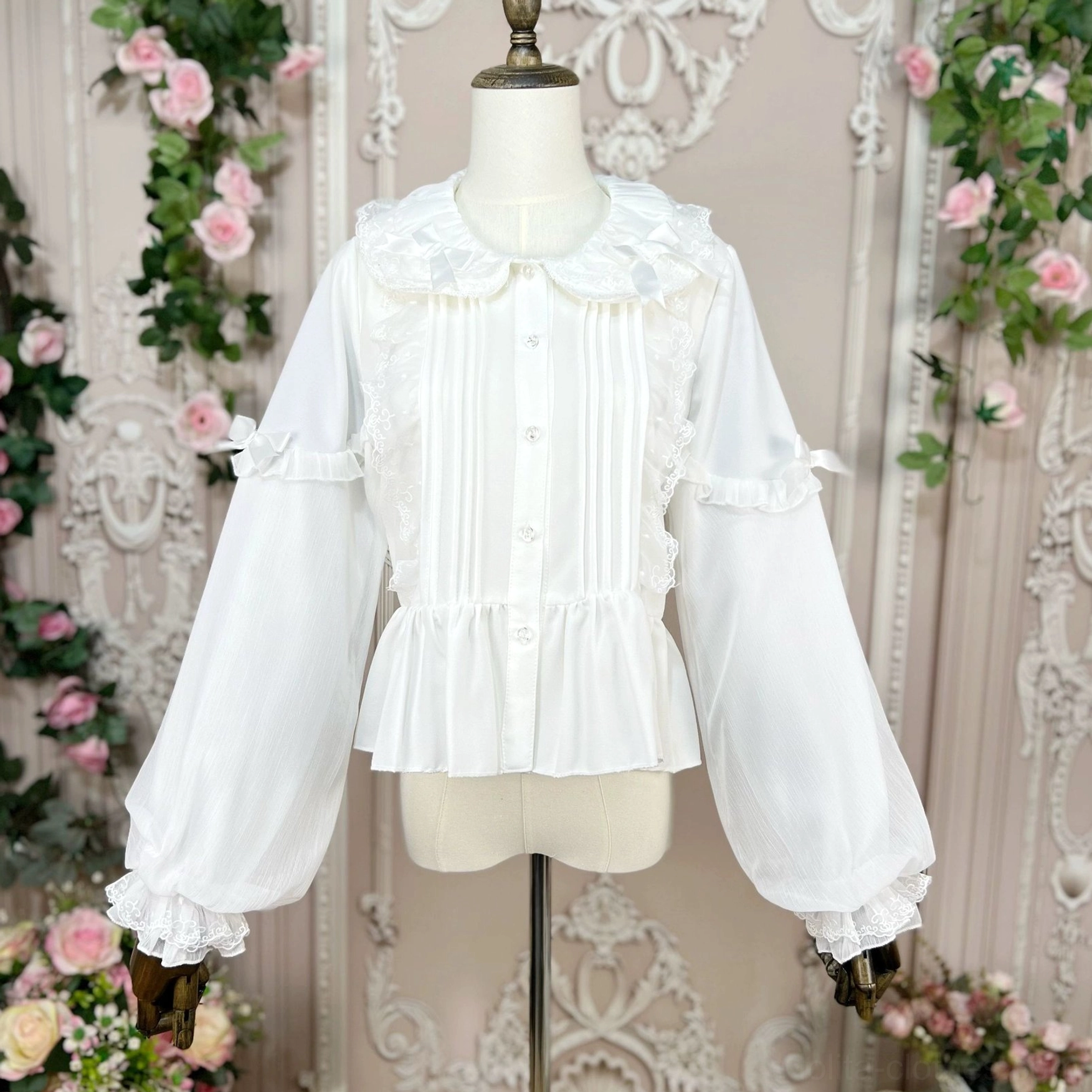 White sweet Lolita puff-sleeve blouse worn on dress form mannequin displaying Peter Pan collar, front lace trim, decorative bows and ruffled hem - front view vintage floral background