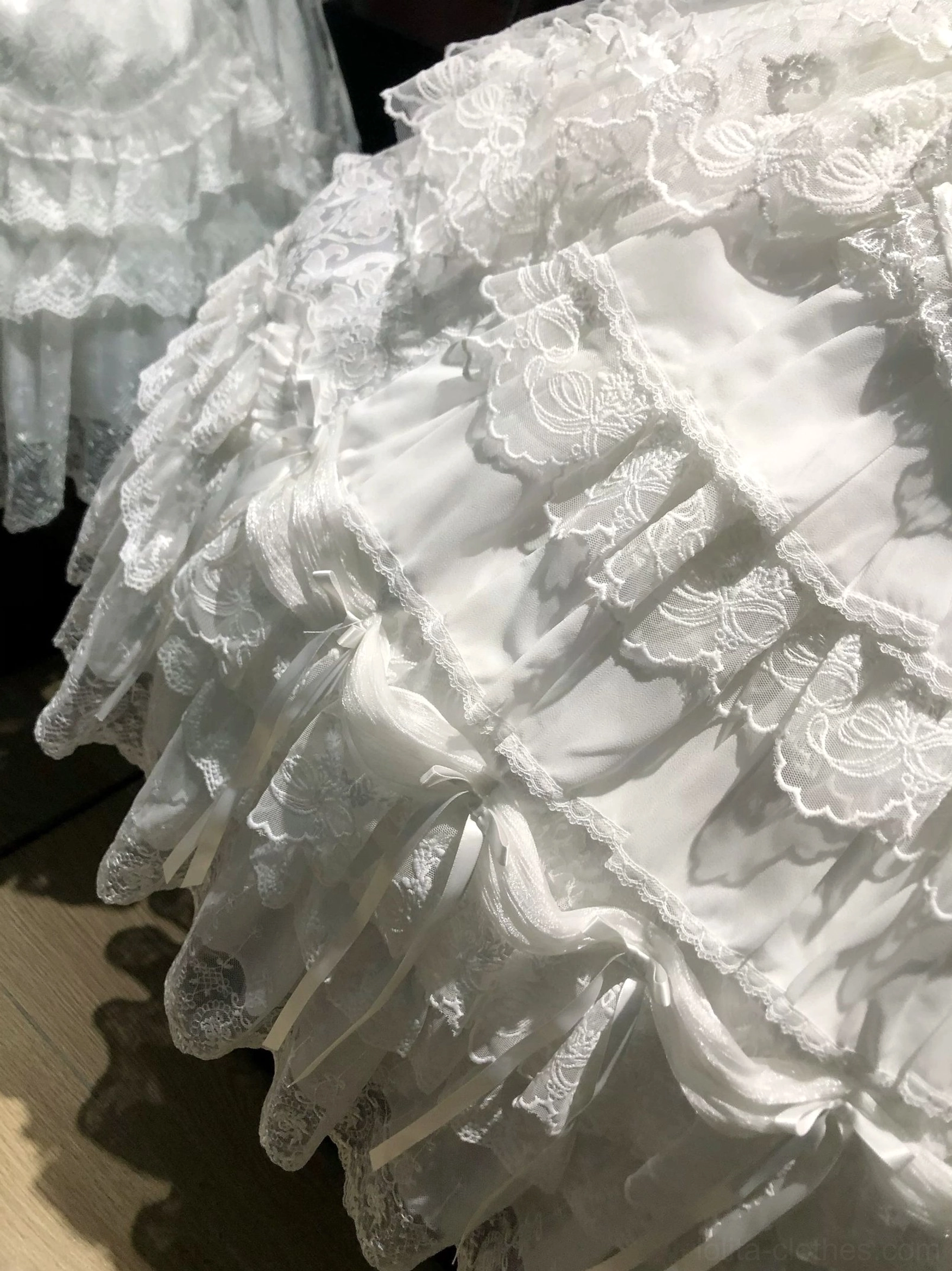 Close-up detail of white sweet lolita tiered dress skirt showing all-white layered lace ruffles intricate embroidered patterns full fluffy design