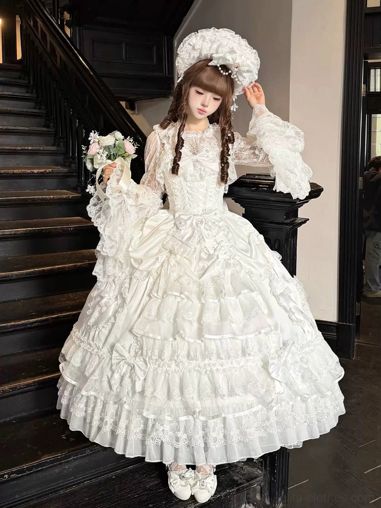White sweet wedding Lolita JSK dress three-quarter side view featuring flared lace sleeves, tiered ruffle skirt with delicate lace trims throughout, worn by brown twin braids model with white fancy headdress holding bridal bouquet