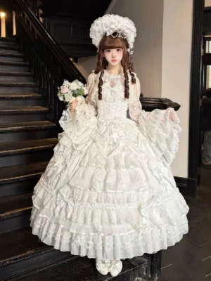 White sweet wedding Lolita JSK dress with multi-layered lace ruffle skirt, high neck lace trim, flared lace sleeves, worn with white bridal fancy headdress and brown twin braids on model holding bouquet on indoor staircase