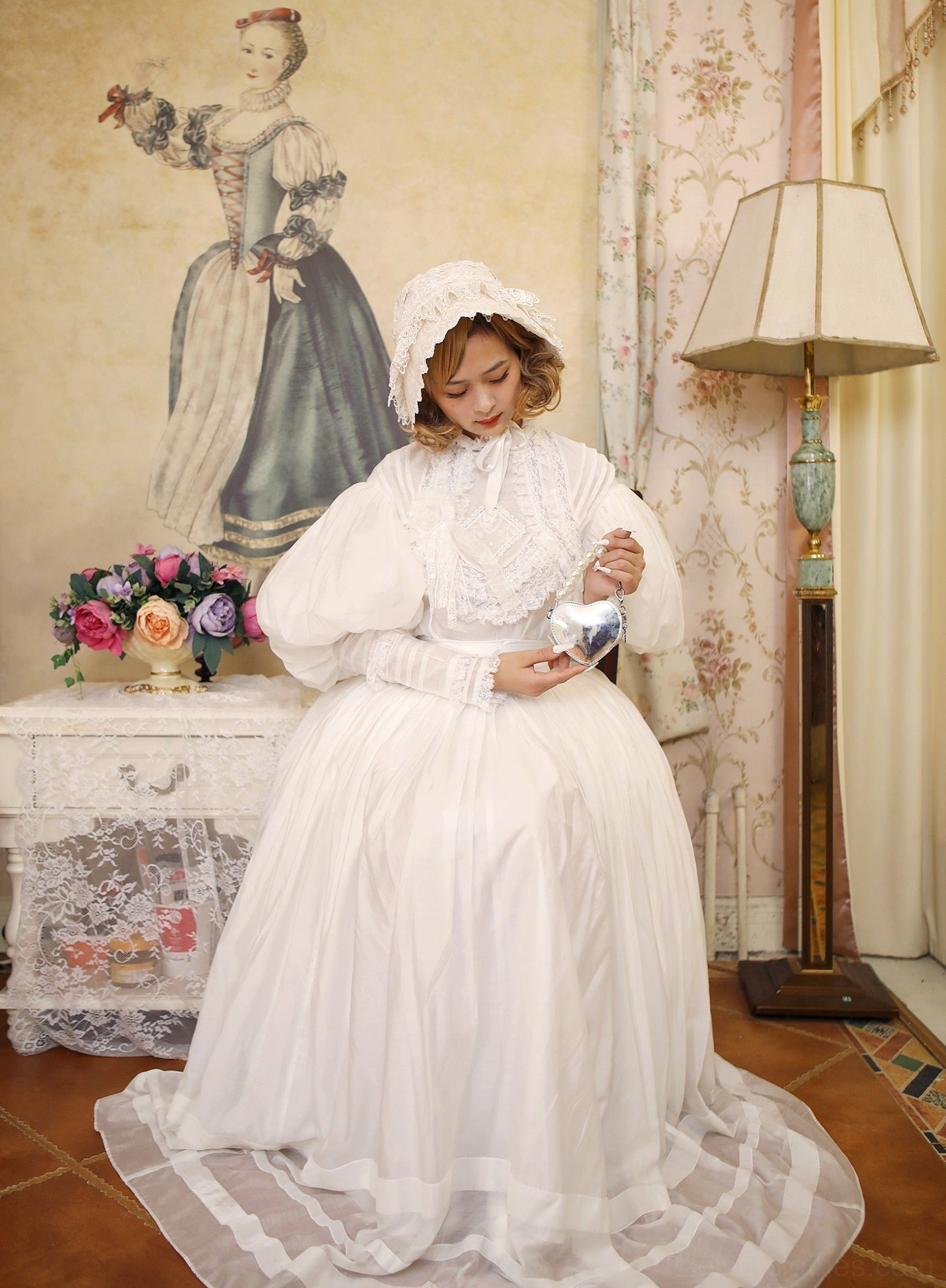 Seated model in white long-train Victorian Lolita dress with matching bonnet, full puff sleeves, high lace collar, floor-length skirt with train in vintage retro parlor interior setting