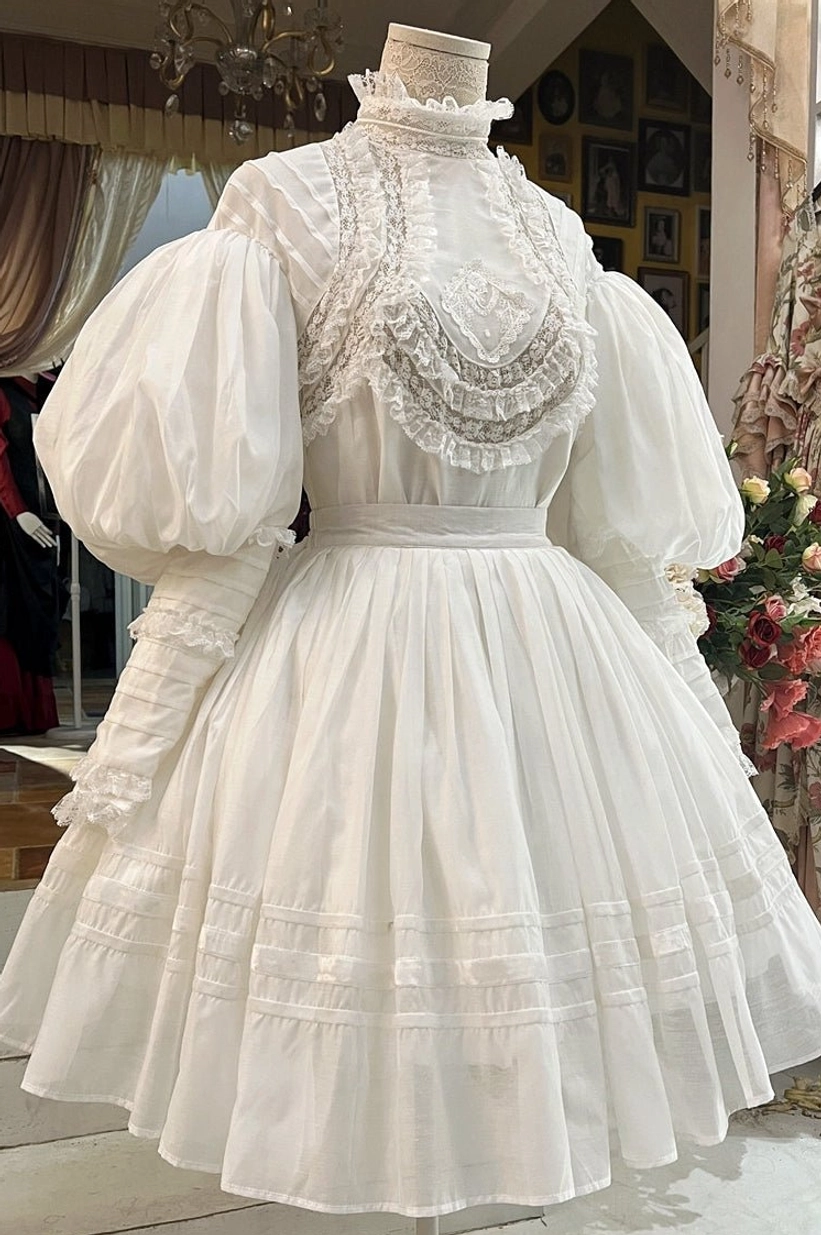 Front full display on dress form of white Victorian Lolita blouse and long skirt set featuring intricate handmade lace bust appliqué, ruffled high collar, oversized puff sleeves, and pleated skirt with horizontal trim bands
