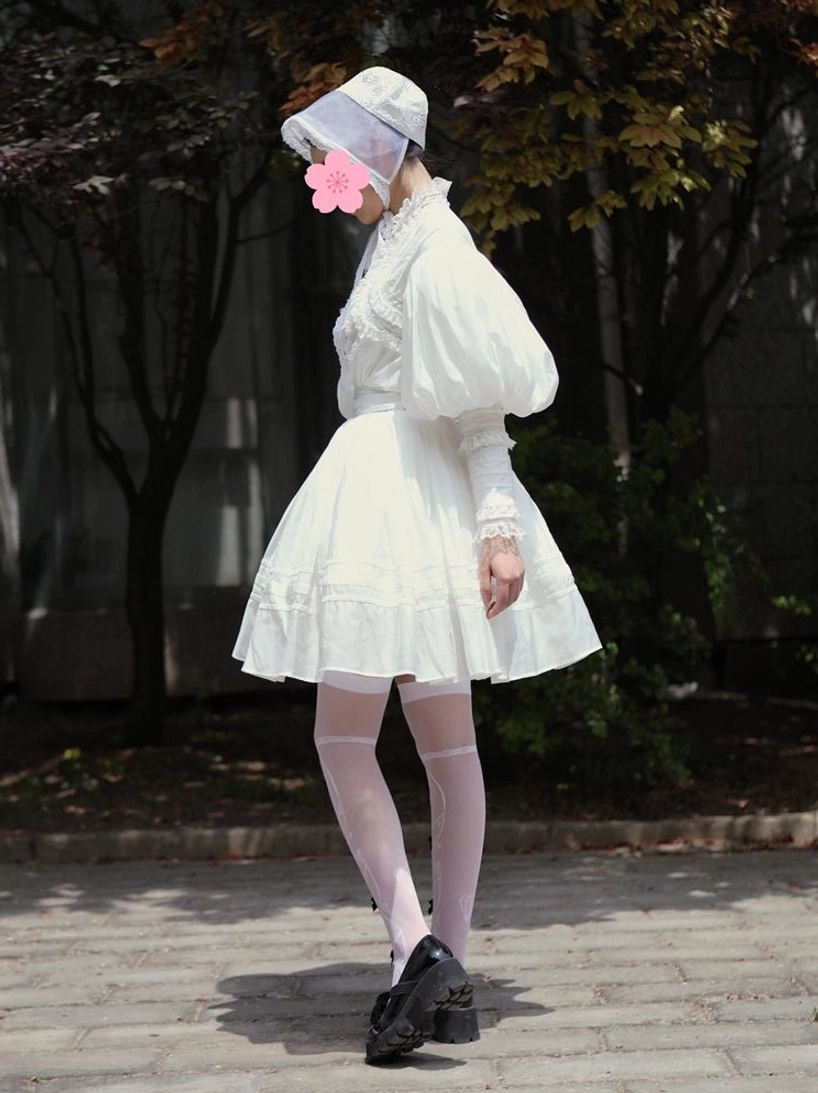 Model walking on paved city street wearing white vintage Lolita two-piece set with white bonnet featuring pink flower ornament, ruffled mini skirt, patterned sheer stockings, and black leather loafers