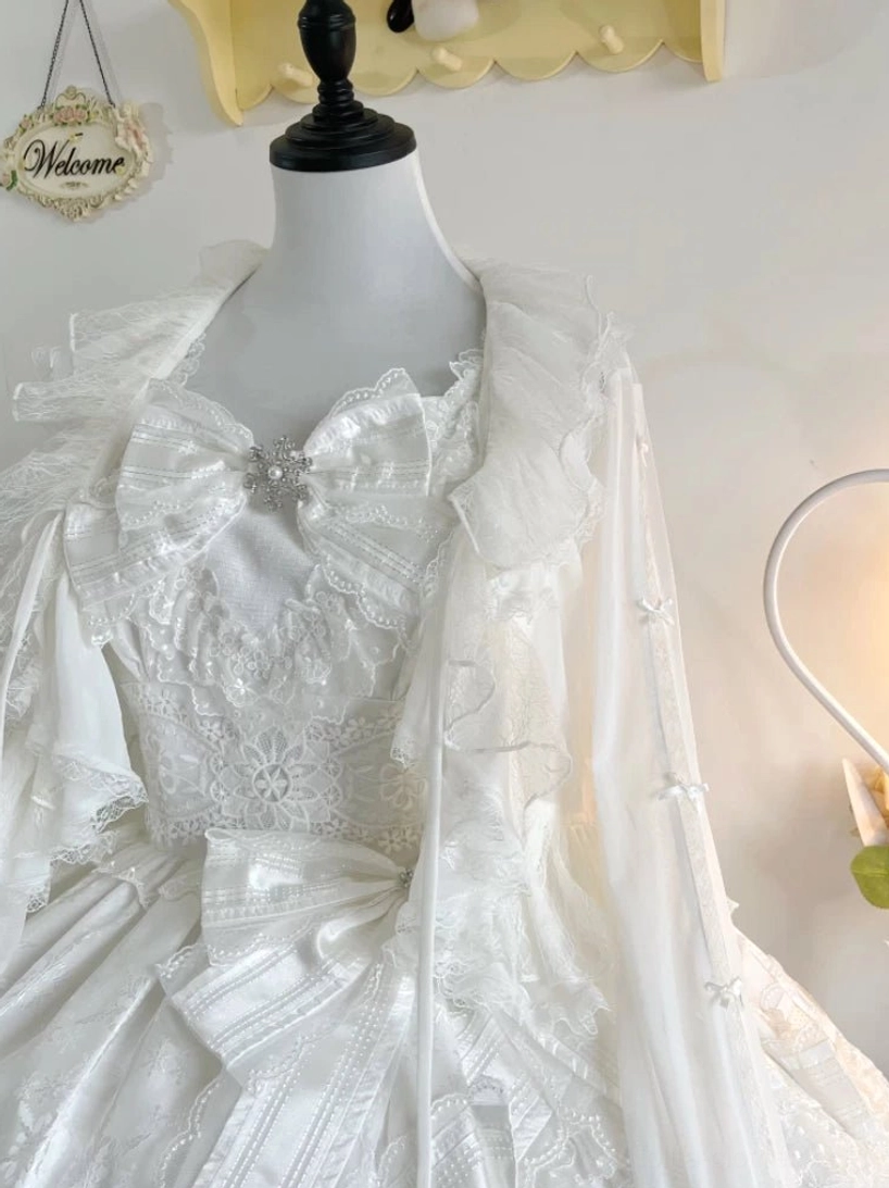 White wedding-style lolita dress set with tulle bolero, large satin bow with gem brooch, sheer bolero with lace ruffle collar over lace bodice front close-up
