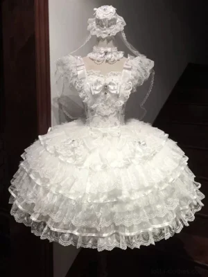 White wedding lolita jumper skirt dress with large bow at neckline, layered lace tulle skirt, sheer tulle accents, and all-white elegant bridal tone on mannequin