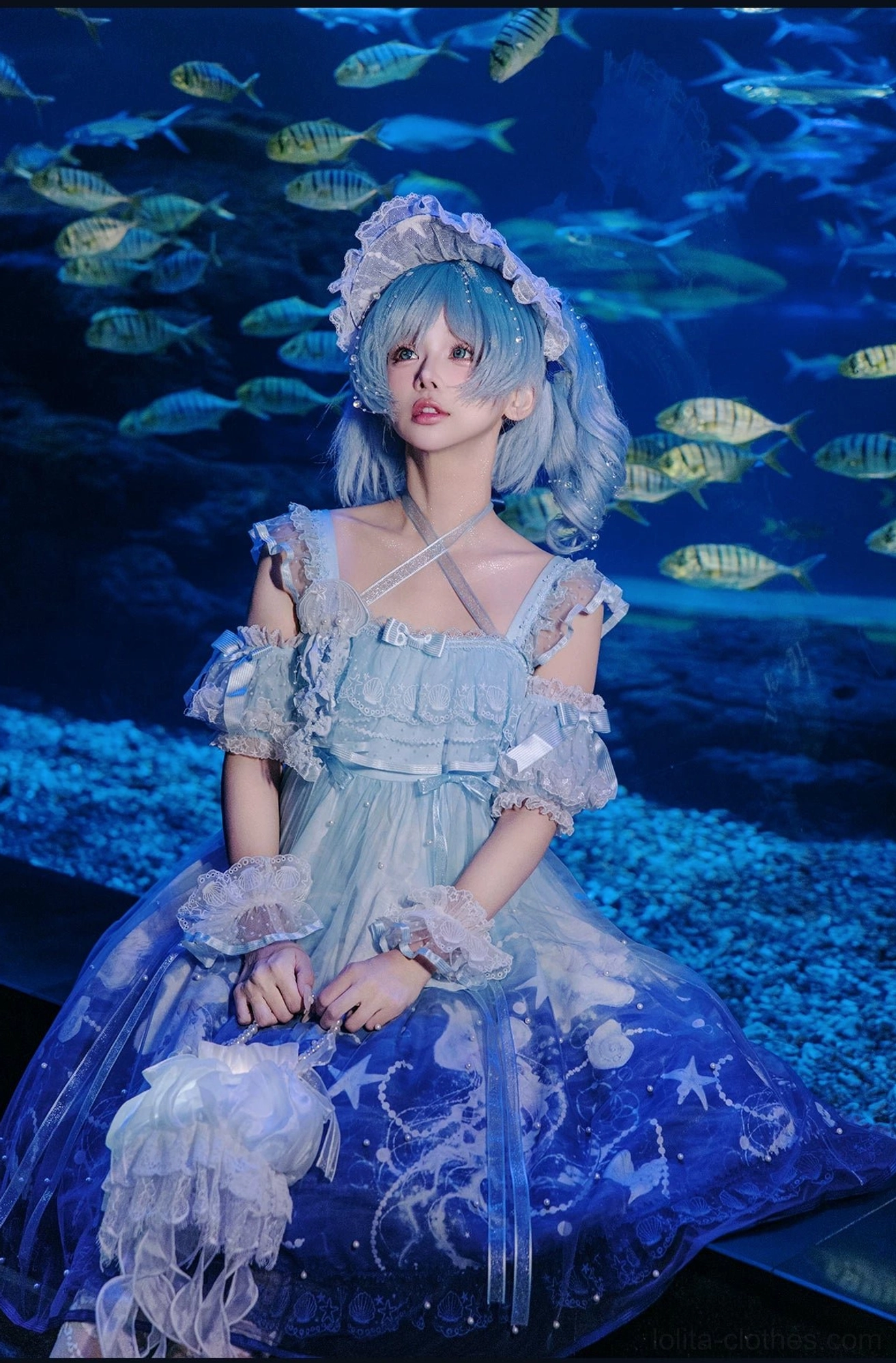 Navy blue gradient jellyfish-themed sweet lolita full-body seated shot featuring off-shoulder ruffled sleeves, matching headpiece, and fluffy pom-pom accessories in underwater setting