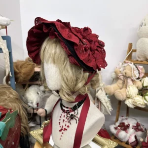 Wine red gothic lolita cotton bonnet hat with ruffled flower trim and neck ribbon, displayed on mannequin three-quarter left side view