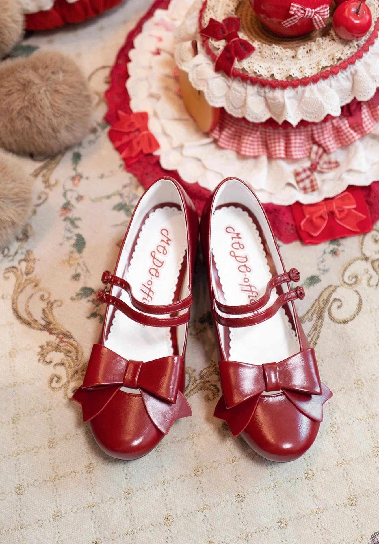Wine red pointed toe Lolita Mary Jane shoes with large front bow and patent leather finish displayed on vintage tabletop with strawberry cake themed retro decor and branded insole