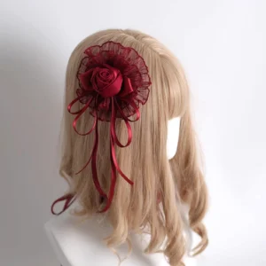 Single wine red rose side hair clip with lace mesh decoration and flowing satin ribbon tails, back three-quarter view on blonde wig mannequin