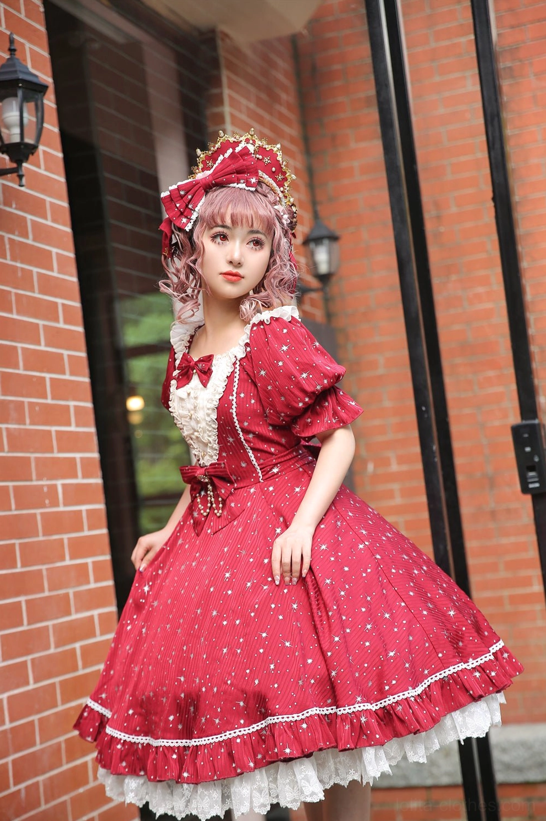 Red wine lolita jumper skirt dress with metallic star foil print white lace trim puff sleeves bow waist full body front view brick building