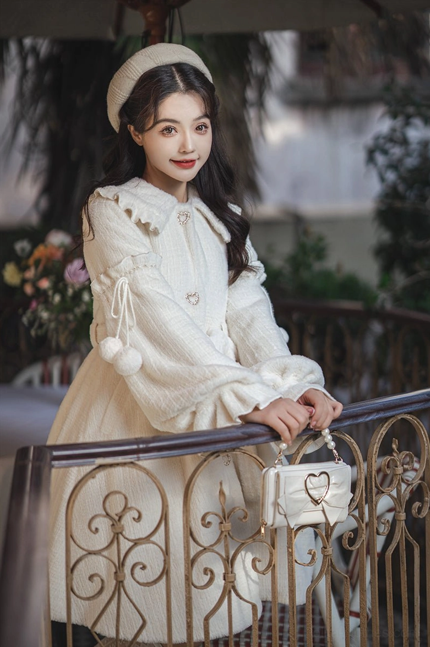 Model leaning on vintage balcony railing wearing cream lolita winter coat with Peter Pan collar, single-breasted button placket, matching beret, and heart-shaped handbag