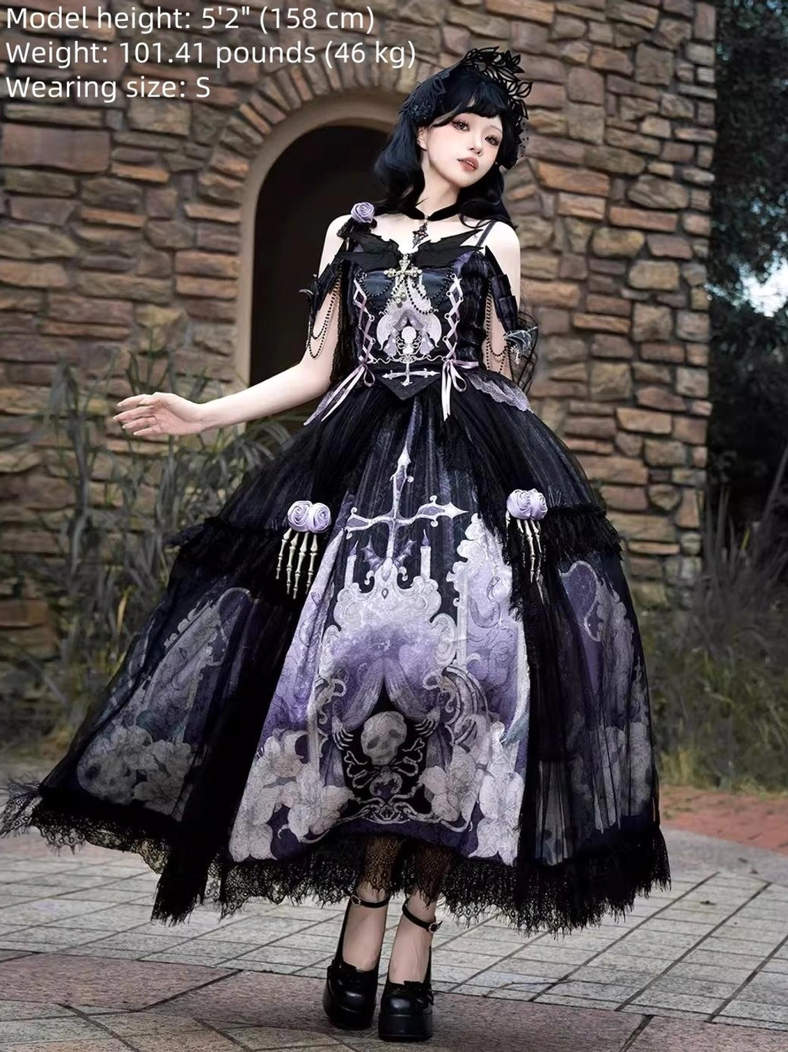 Withered Bone Gothic Lolita dress on model front three-quarter wearing size S matching gothic prints lace tulle hemline cold shoulder strap design black curly-haired model height 5-foot-2-inches outdoor stone arch courtyard