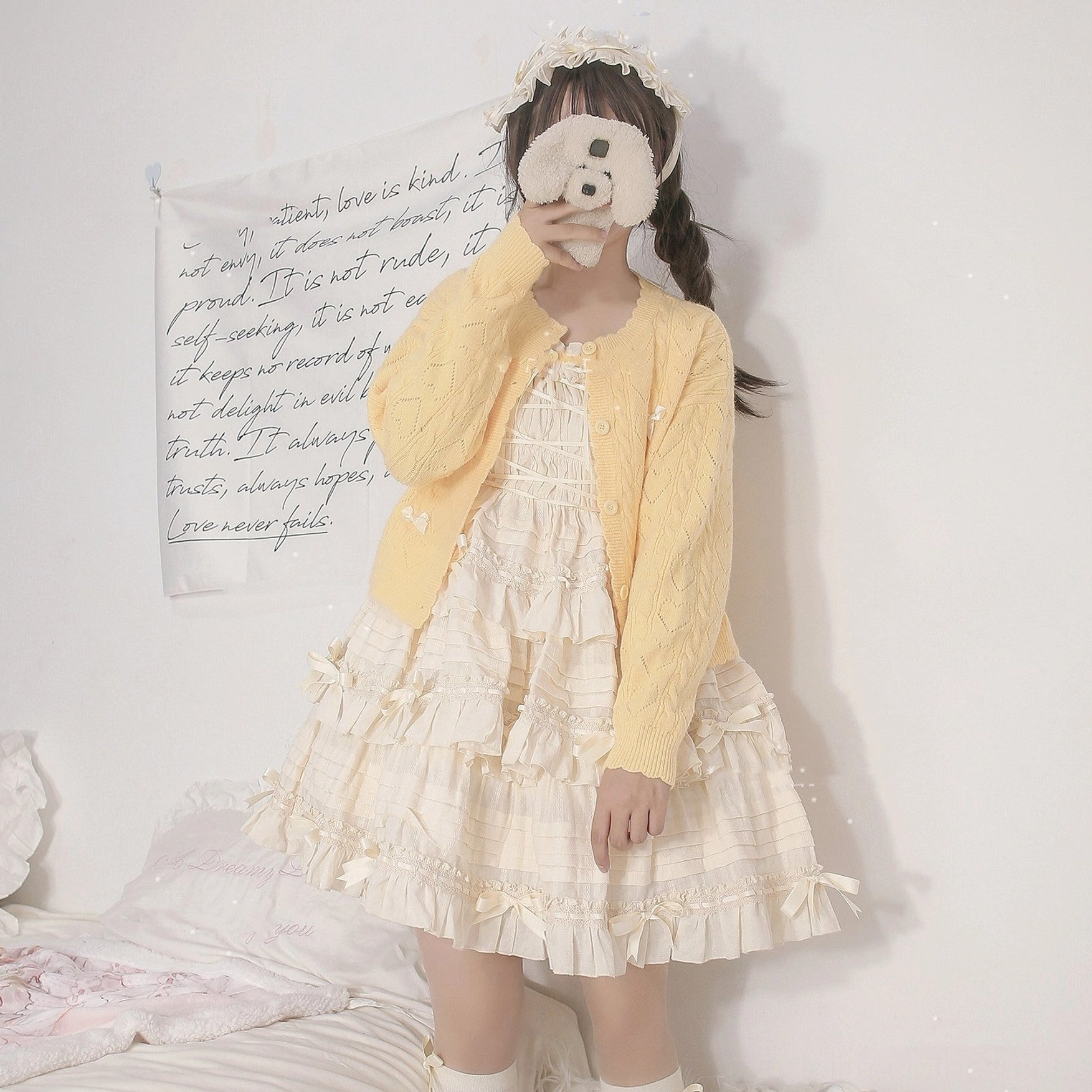 Yellow hollow out long sleeve Lolita cardigan with cable knit texture and button closure paired with ivory tiered Lolita dress, model with plush toy, bedroom tapestry background