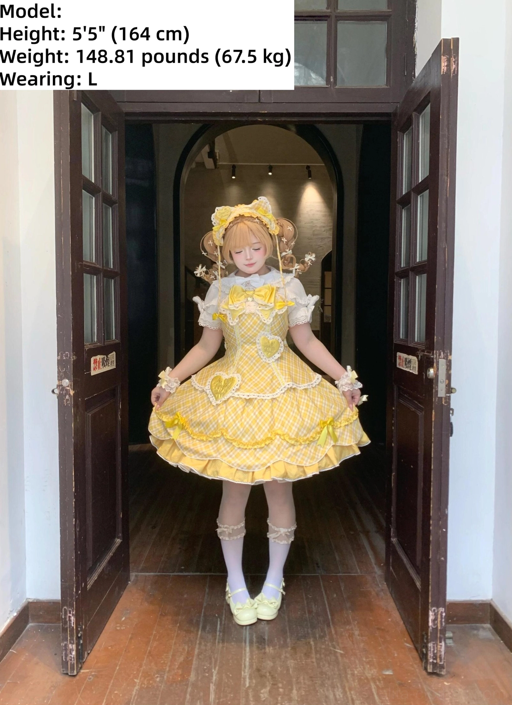 Yellow plaid sweet lolita OP one-piece dress front full-body single model view featuring gingham fabric with heart-shaped front decorations, ruffled lace trims and cross collar tie, white socks and light green flat shoes, vintage wooden door hallway setting