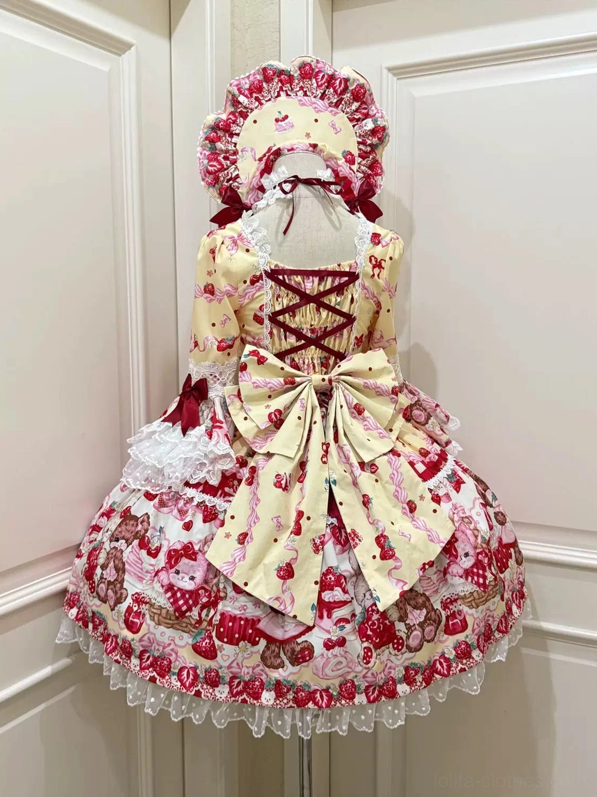 Yellow-based strawberry bear lolita OP dress back view on mannequin showing crisscross lace-up back, large satin waist bow, ruffled skirt hem with white lace trim and bonnet